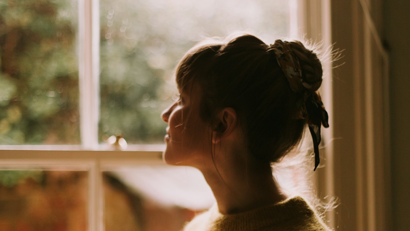 A woman looking out of a window in soft evening light