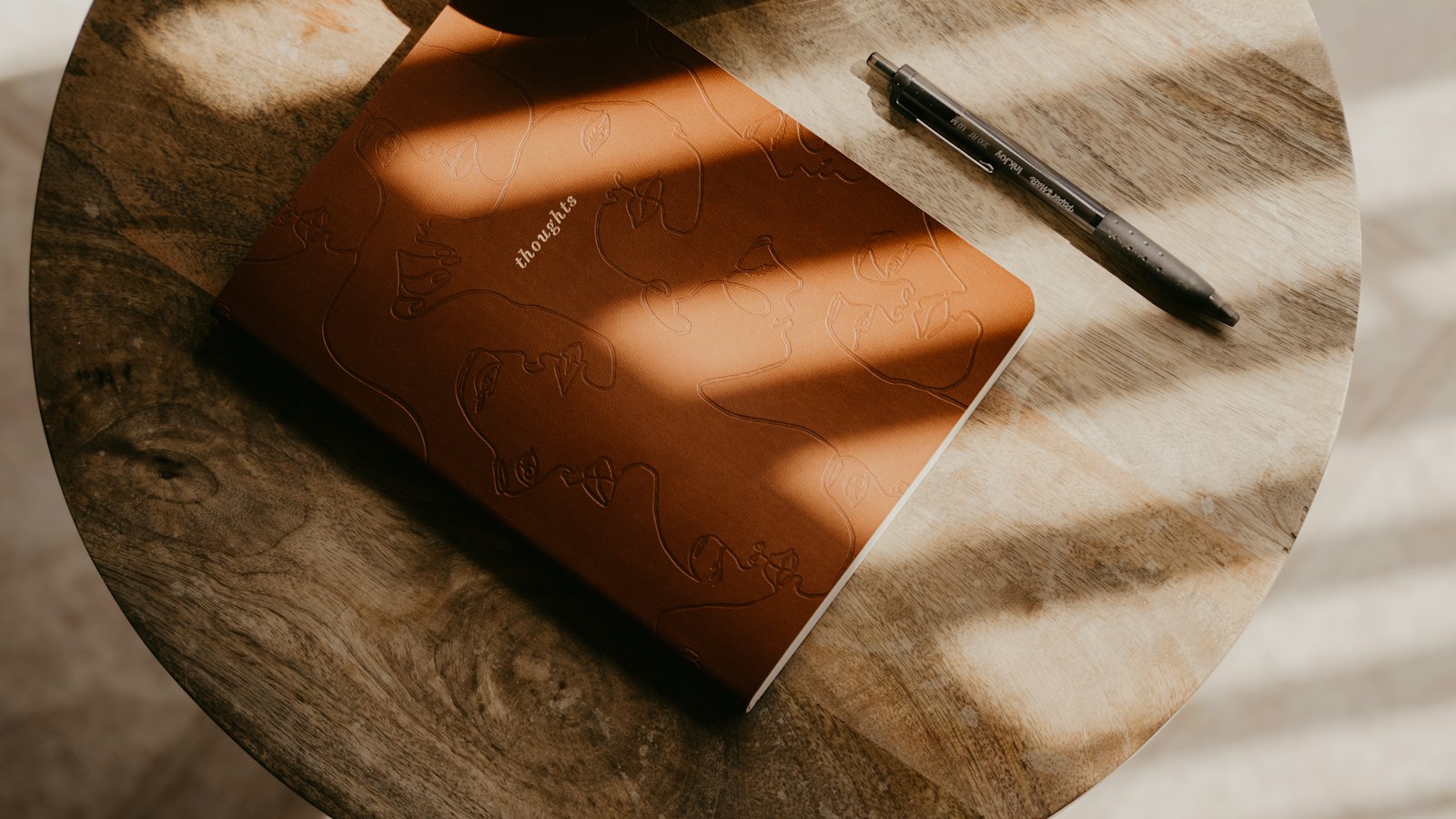 A notebook and a pen on a sunlit wooden table